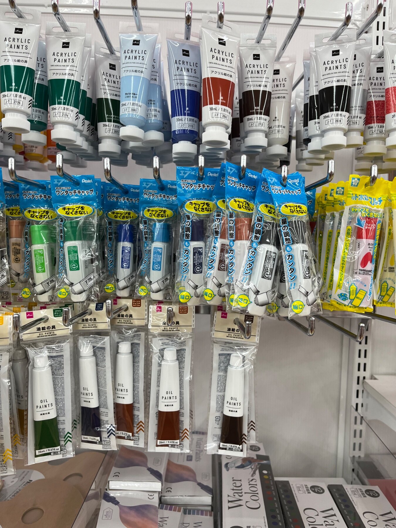 ダイソー 東戸塚の電池・電気小物売り場に並ぶアクリル絵の具、ワンタッチキャップ（絵の具用）など計3商品（2026年8月11日撮影）