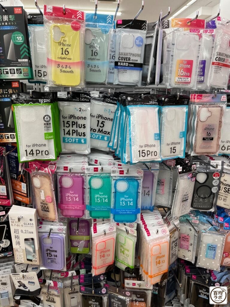 ダイソー 東戸塚のスマホ用品売り場に並ぶ強化ガラス保護フィルム（iPhone 15 Pro Max、ブルーライトカット）、さらさらケース（iPhone 16）など計20商品（2026年8月14日撮影）