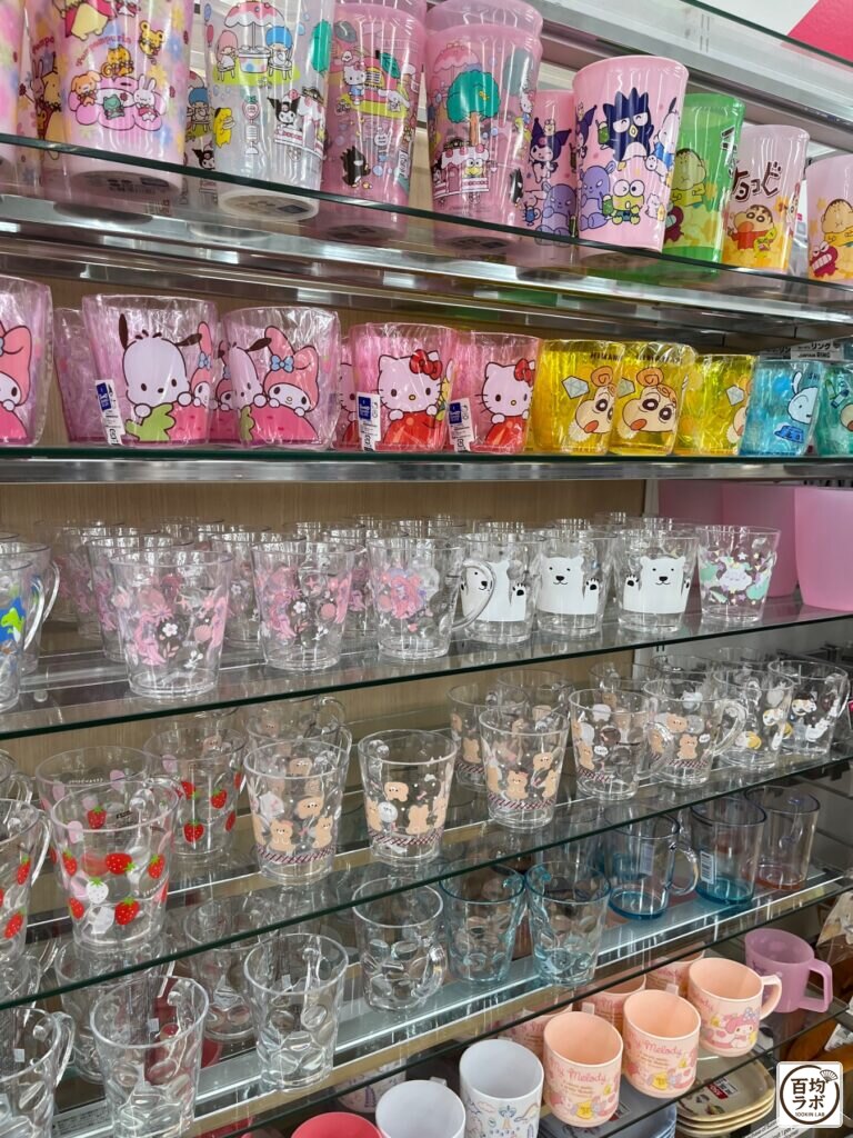 ダイソー 東戸塚のキッチン売り場に並ぶサンリオキャラクター柄プラスチックコップ、クレヨンしんちゃん柄プラスチックコップなど計10商品（2026年8月14日撮影）